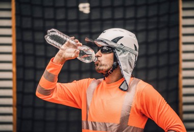 Ein Arbeitnehmer trägt Kleidung zum Schutz gegen Hitze und trinkt Wasser aus einer Flasche. Ein Arbeitnehmer trägt Kleidung zum Schutz gegen Hitze und trinkt Wasser aus einer Flasche.