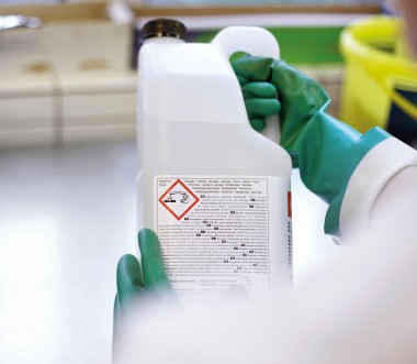 Eine Person mit Schutzhandschuhen schaut sich einen Behälter mit Gefahrstoffkennzeichen an.